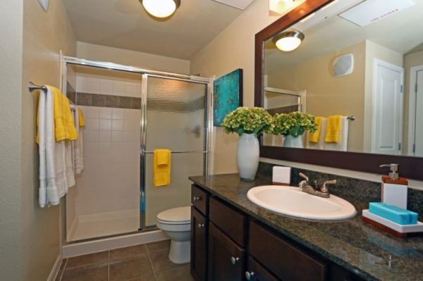 Bathroom with ceramic tile flooring, walk-in shower, toilet, and large vanity with granite countertops and dark wooden accents