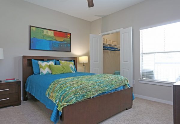 Bedroom with plush carpeting, full bed, nightstands, ceiling fan, large window, and walk-in closet
