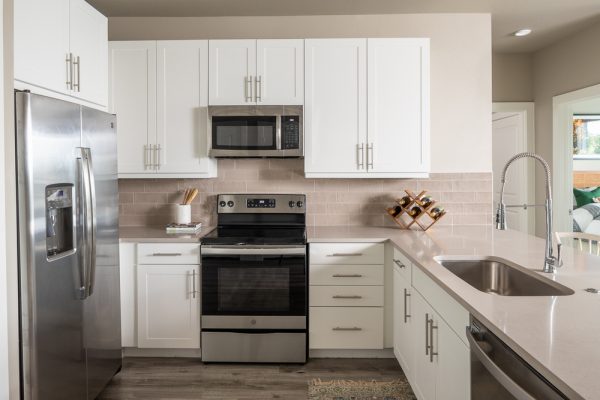 Gourmet kitchen with quartz countertops, designer white cabinetry, kitchen island, and stainless steel appliances including a side-by-side fridge, built-in microwave, stove, oven, and dishwasher